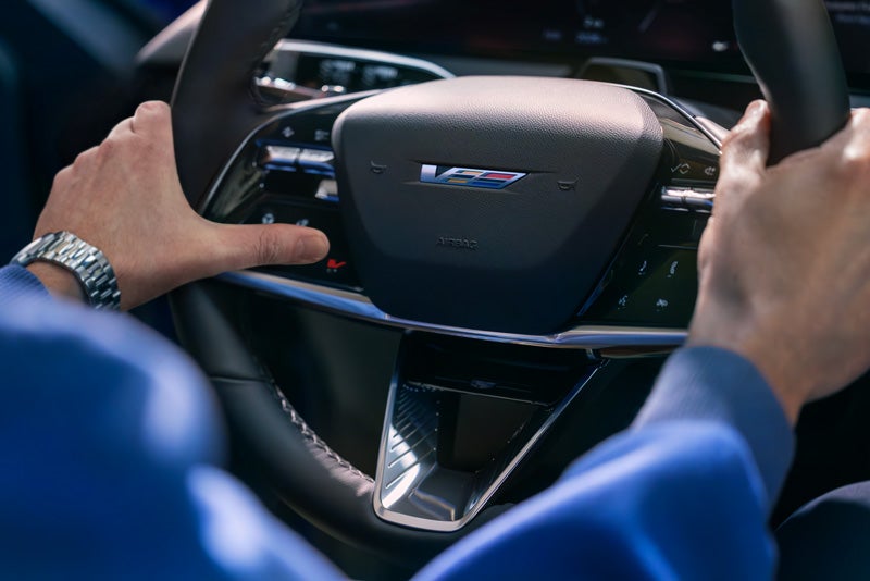 Close-up of a Man About to Press the V-Button on the 2026 OPTIQ-V Steering Wheel | Lynn Layton Cadillac in Decatur AL